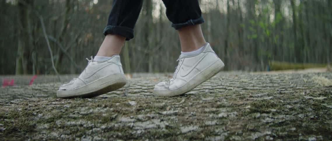 White tennis shoes walking across a log in the woods