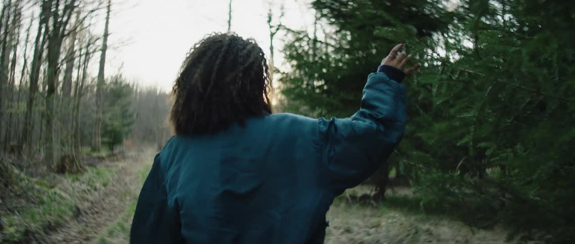 A black woman wearing a jacket strolls down a path in a forest