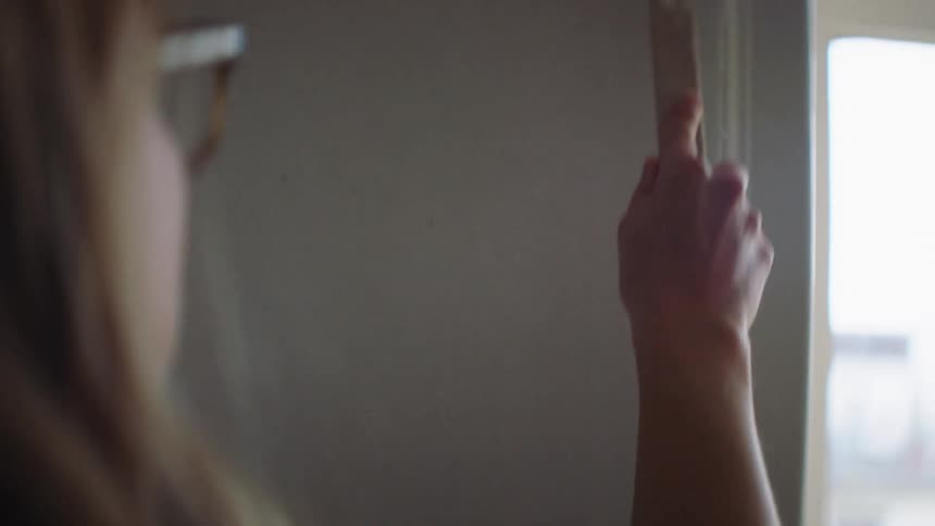 A white woman paints the wall by a door frame in her home