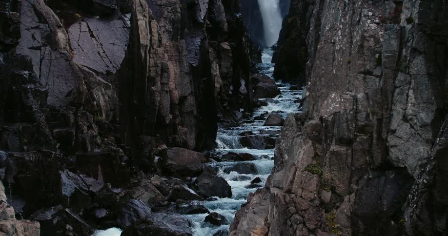 A large waterfall dumps water into a raging river running through a deep canyon