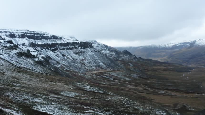 Aerial view of mountain range covered in snow under a cloudy sky