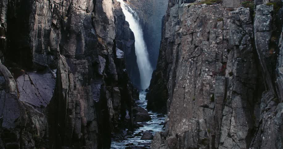 A waterfall fills a raging river that runs through a rocky canyon