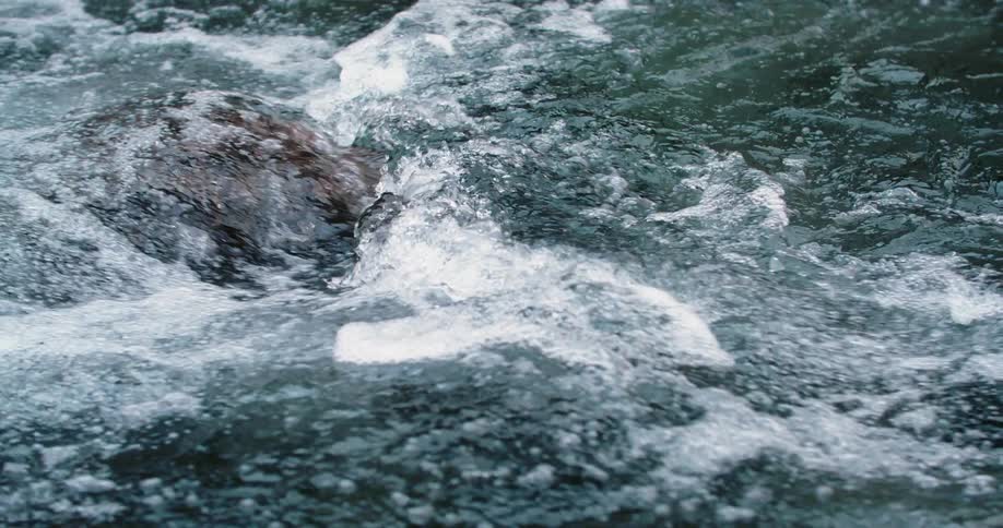 Water flowing two direction clashes over rocks creating white foam and bubbles