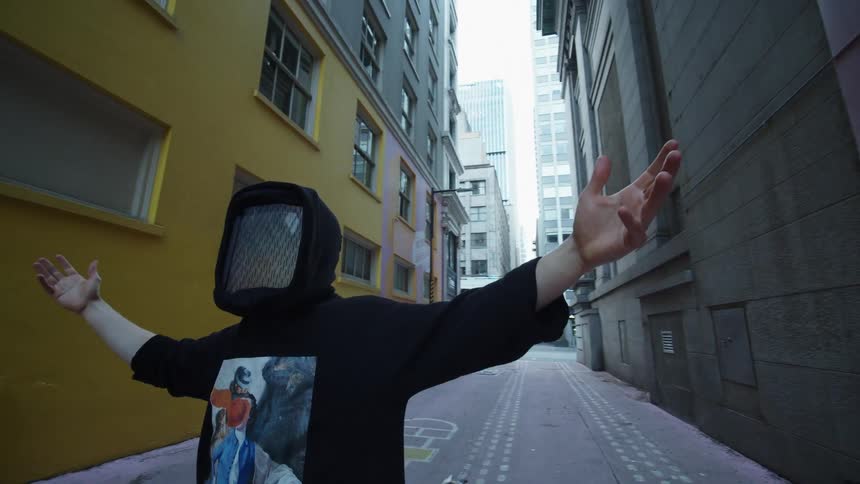 Person wearing flickering digital mask poses in alley with arms outstretched