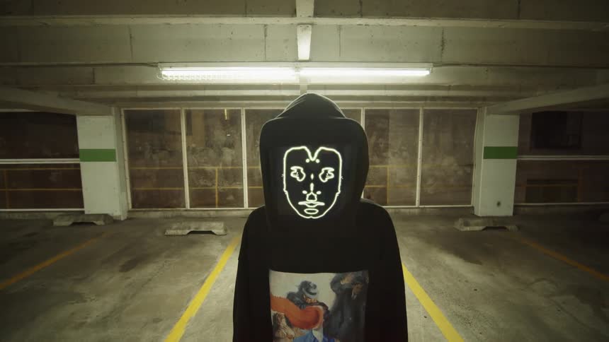 A person in a costume with a screen for a face stands in a parking garage