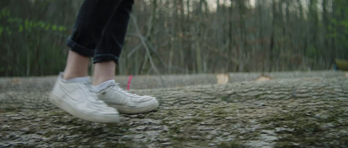 A white person walks on a log in the forest