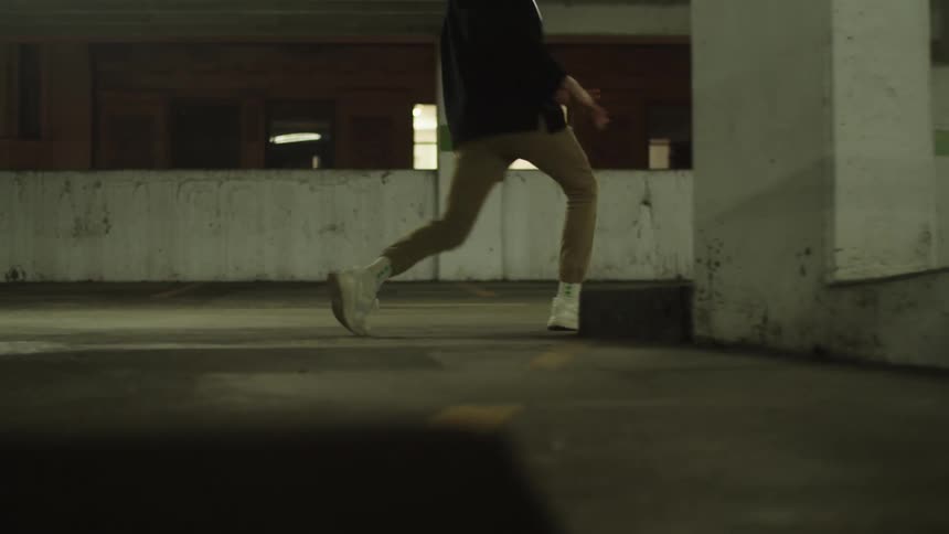 A person in white sneakers dances and spins while walking through a parking garage