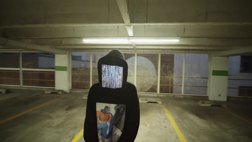 Person wearing square animated digital mask stands in parking garage