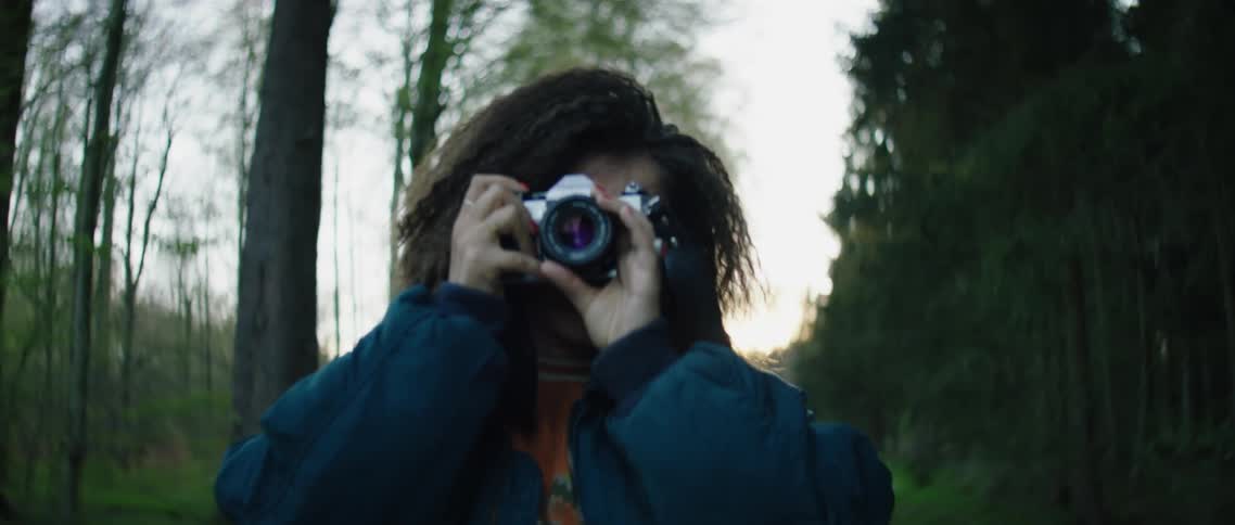 A woman with a camera taking pictures on a dirt path