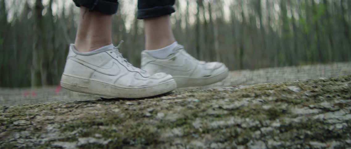 Person in old white tennis shoes walks across fallen log