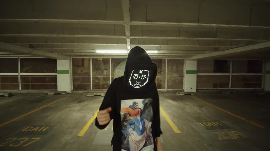 A rapper with a digital screen for a face raps and dances in an indoor garage