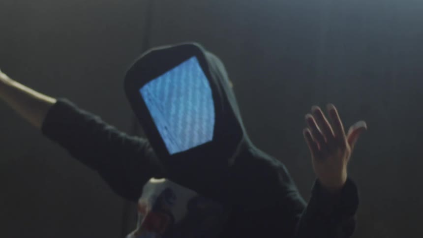 A teenager with a screen in place of his face dances in a parking garage