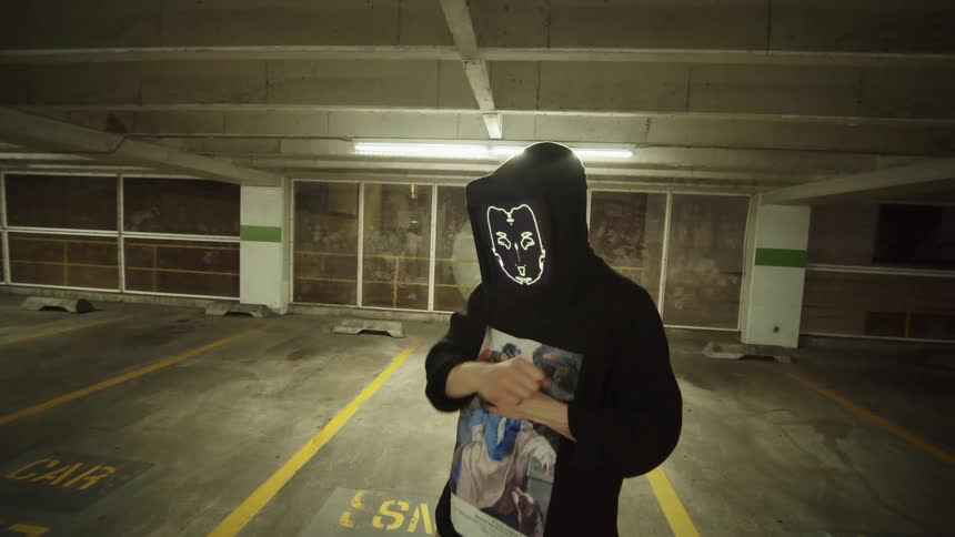 Performer in digital animated face mask dancing in parking garage at night