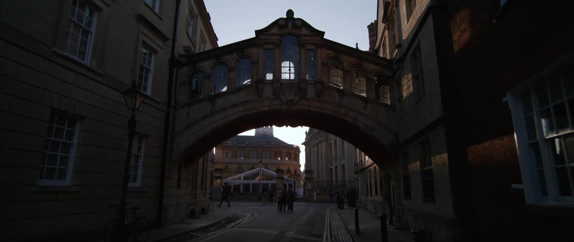 Pedestrians standing in a city street under Hertford Bridge at sunset