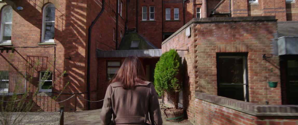 Woman walks briskly towards massive brick building