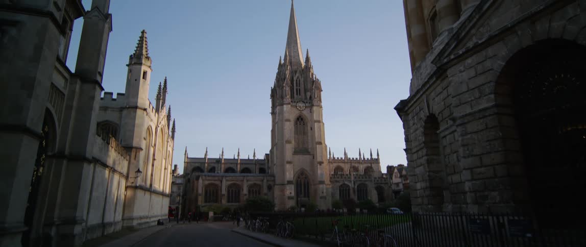 A bird flying in front of a large cathedral with multiple buildings on a sunny day in Oxford