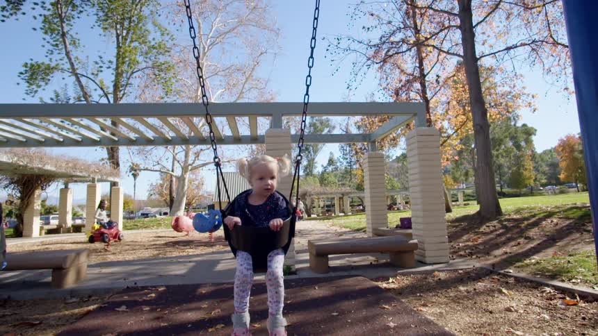 A father pushes his little girl in a swing at a playground