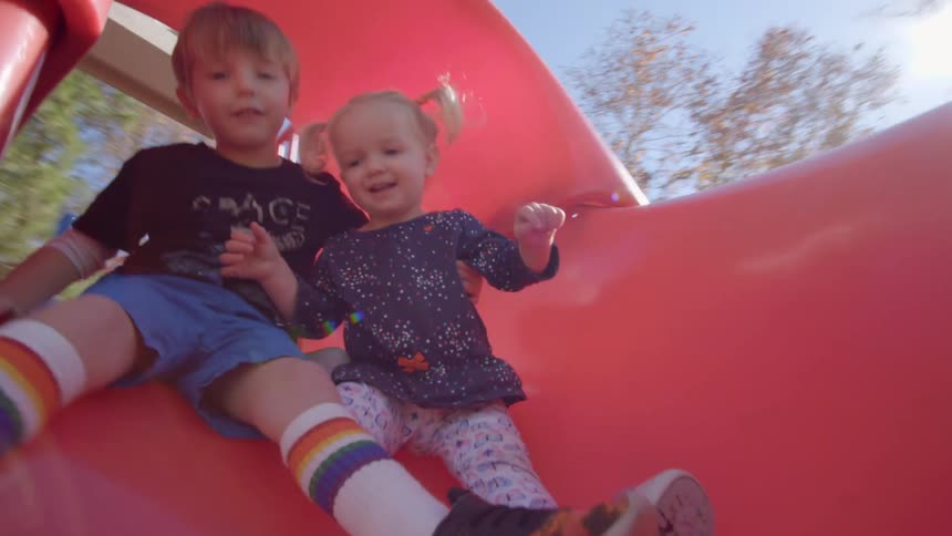 A brother and sister go down a playground slide together