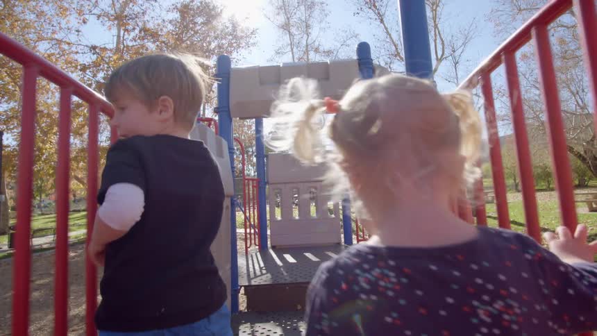 Two small toddlers run together on playground equipment