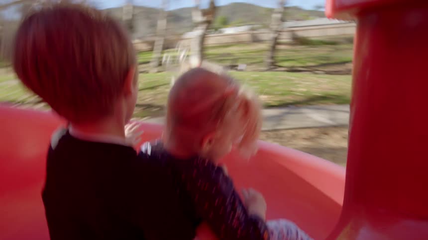 A young boy holds his sister as they go down a slide