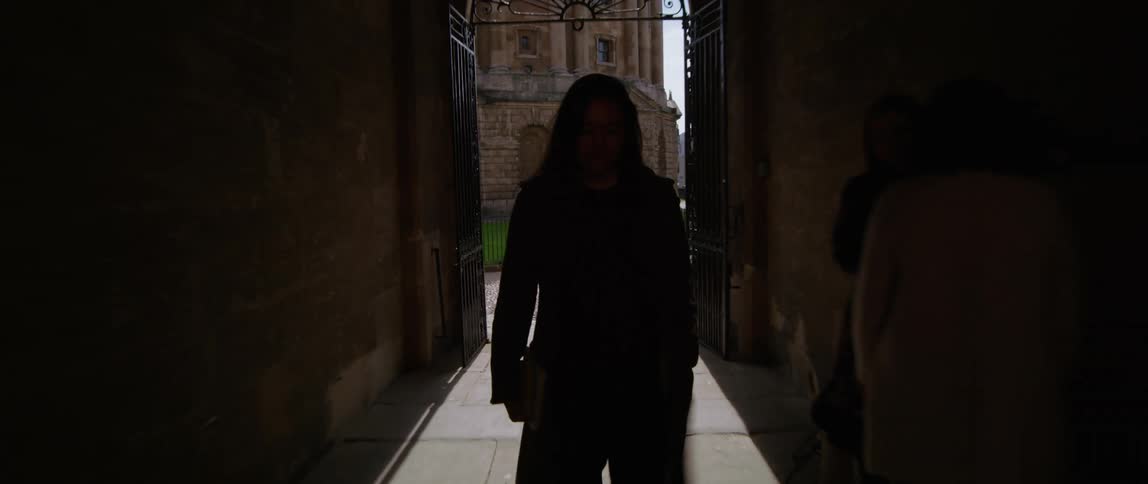 A white woman walks through a narrow alleyway into the courtyard of a university
