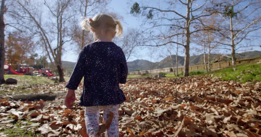 A little girl walks through leaves towards a playground