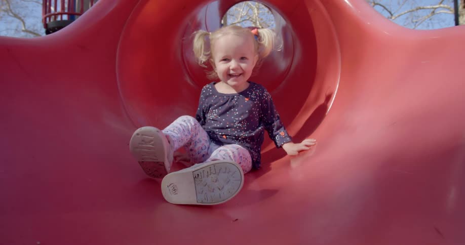 A young girl slides down a red slide at a park