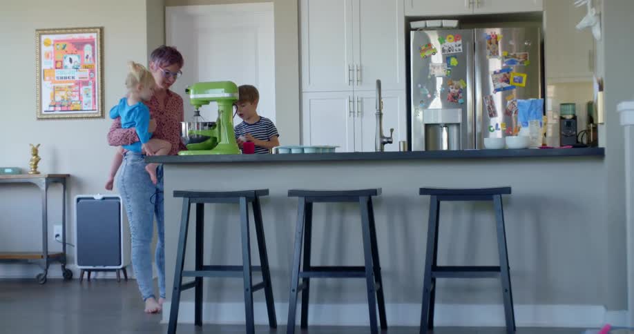 A woman holding her young daughter while her son helps her to fill a mixing bowl
