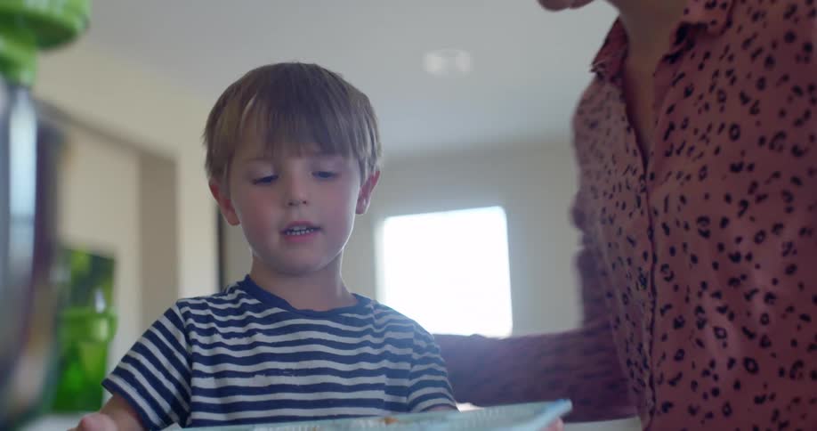 Mother and young son using cupcake tray in kitchen