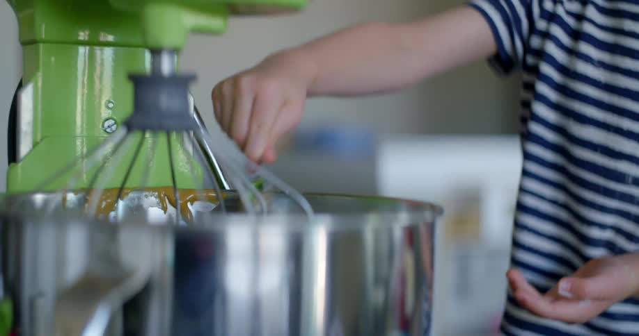 A child puts a spoonful of ingredients in the mixer bowl