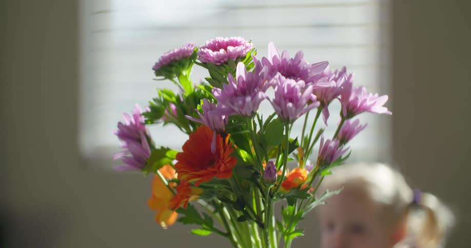 Bright bouquet of flowers is held with blonde girl and window in background