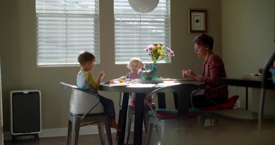 A teenage boy teaches his younger siblings as they sit around the kitchen table