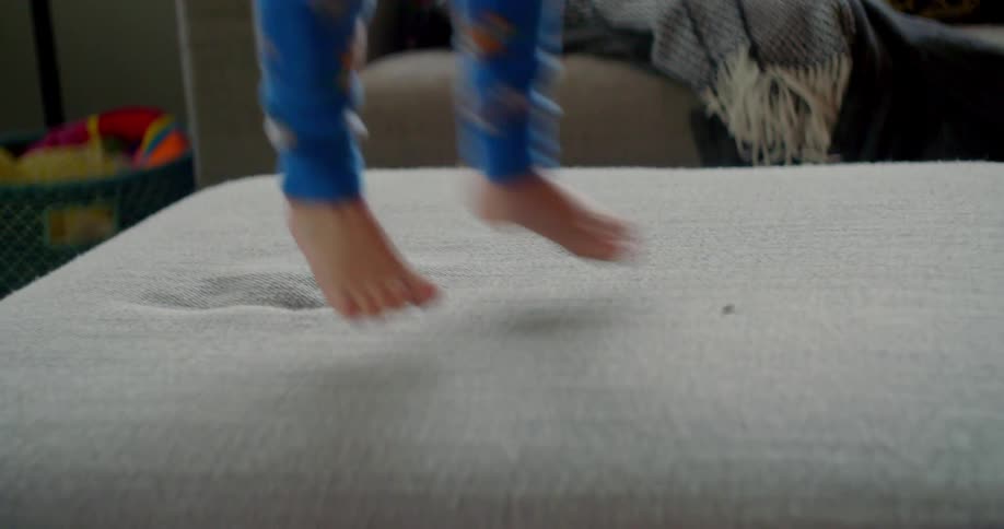 A child in their pajamas jumping on a cushioned footstool