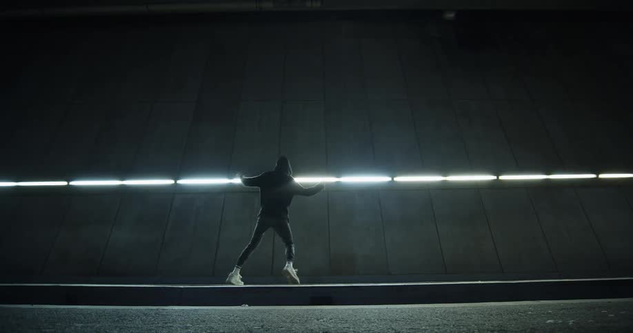 Person dancing in front of building and fluorescent lights at night