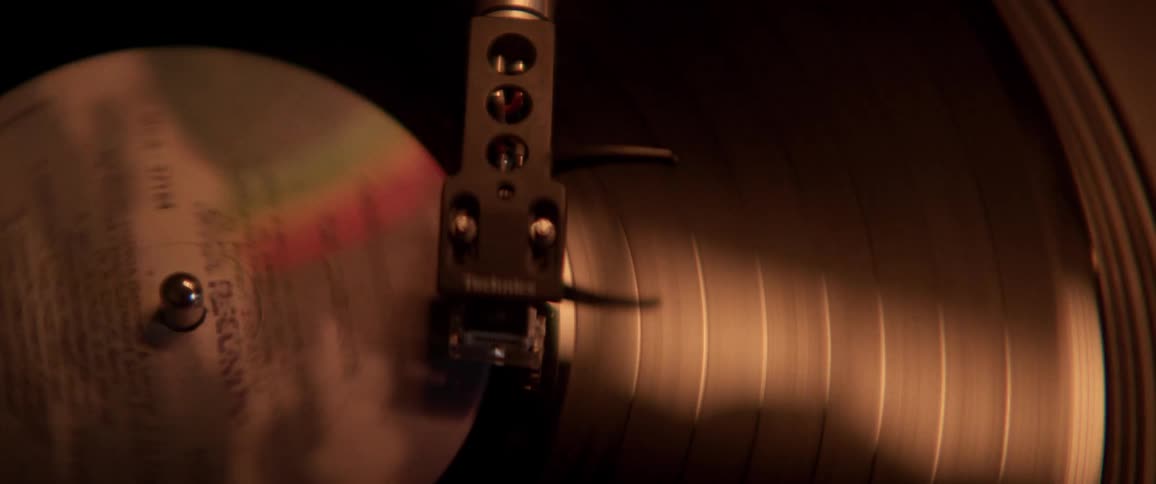 Arm of a record player sits on a record as it spins