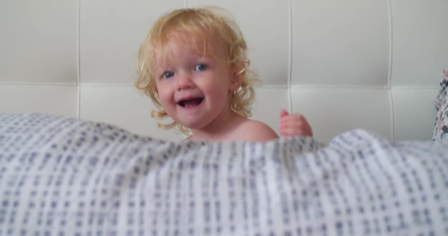 A baby jumping playfully on a sofa before turning to look towards the camera