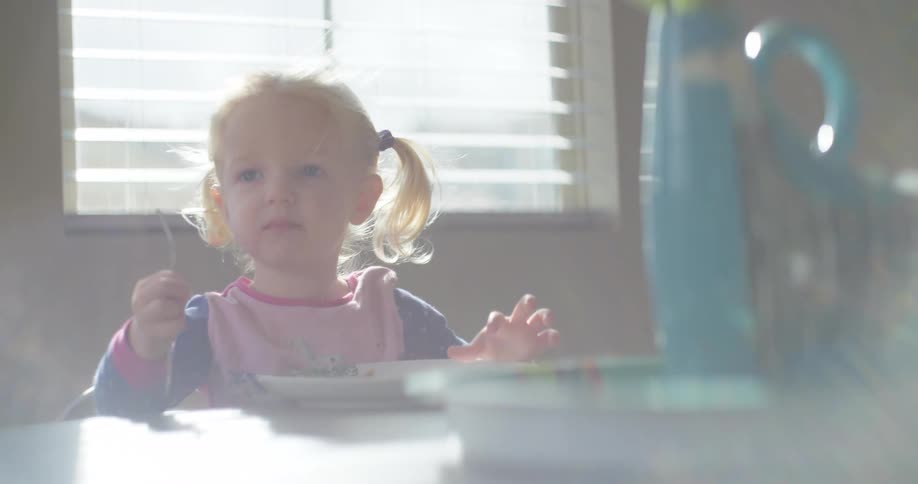 A white toddler sits at a table and eats a meal