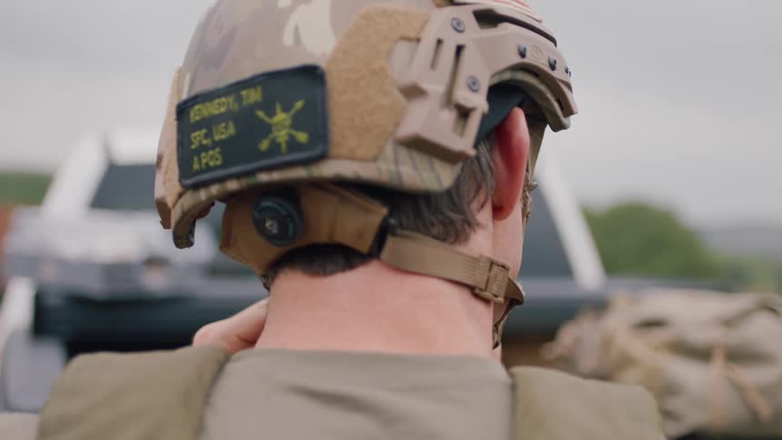 Back of an us soldier outdoors putting a helmet on