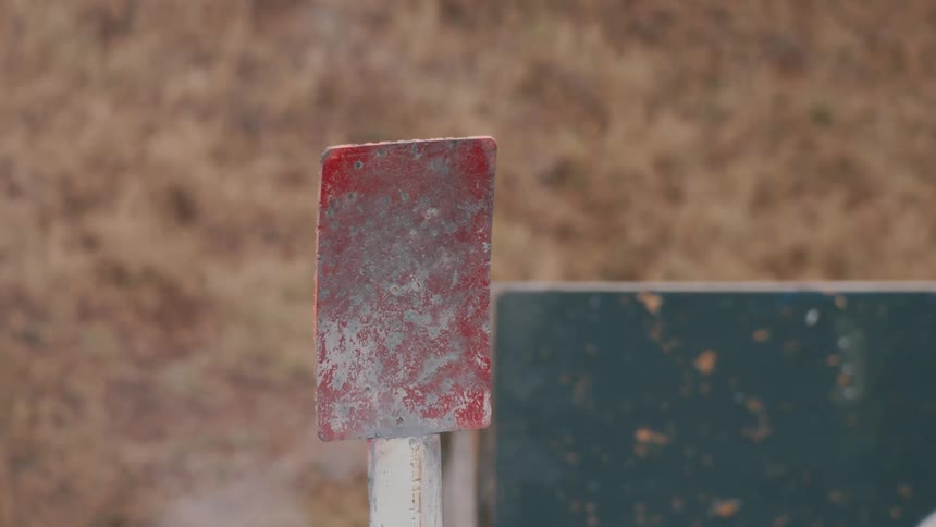 Dust flies from shaking metal sign standing outdoors near brown grass