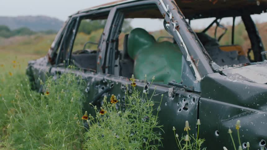 Abandoned old car full of bullet holes in field