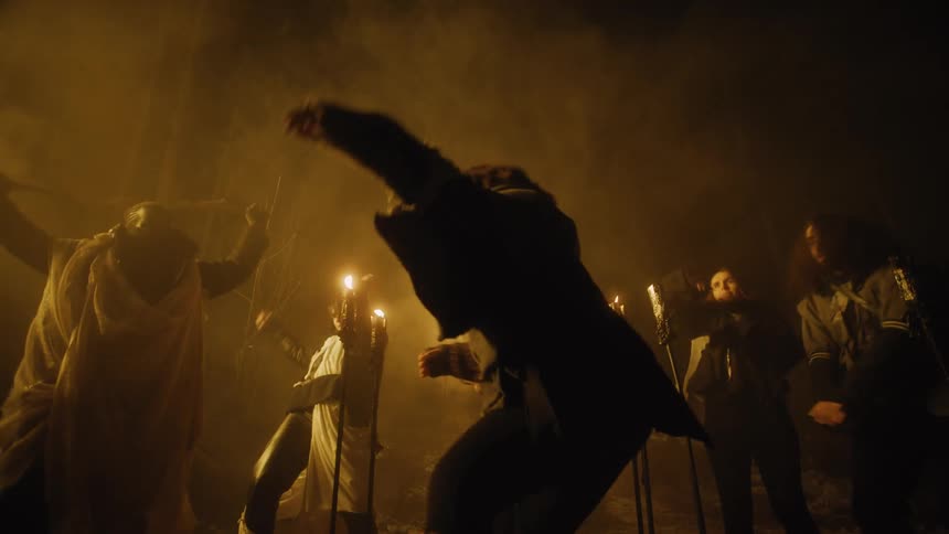 People in costumes dance in the mist outdoors at night with torches