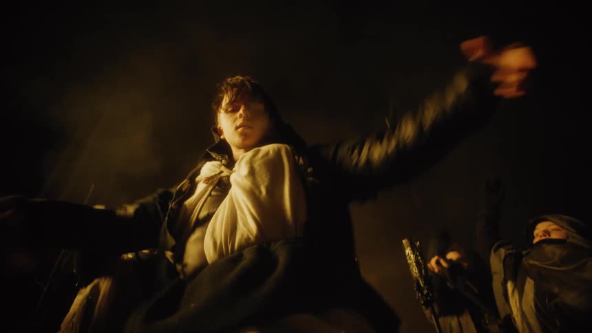 A group of young people in cloaks dancing in a woodland at night by candlelight