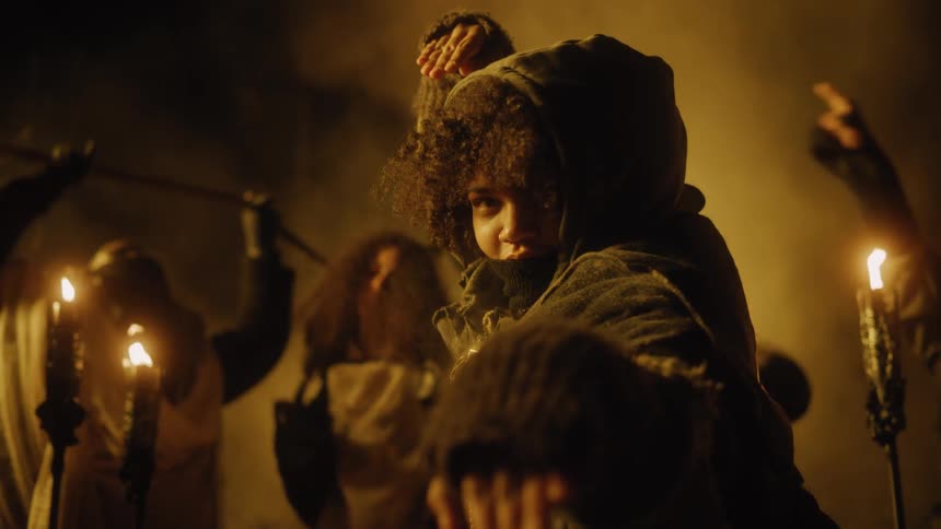 A woman with a fighting pose as people in the background dance next to torches