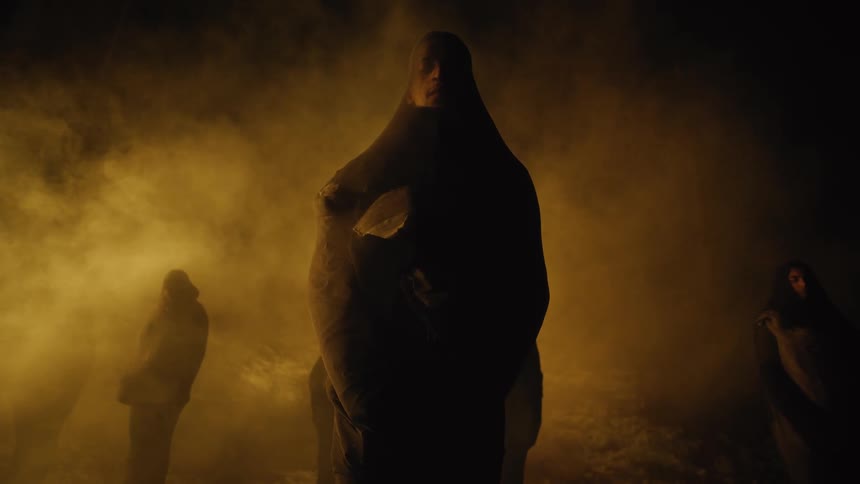 A person standing wrapped up like a mummy with people and smoke in the background