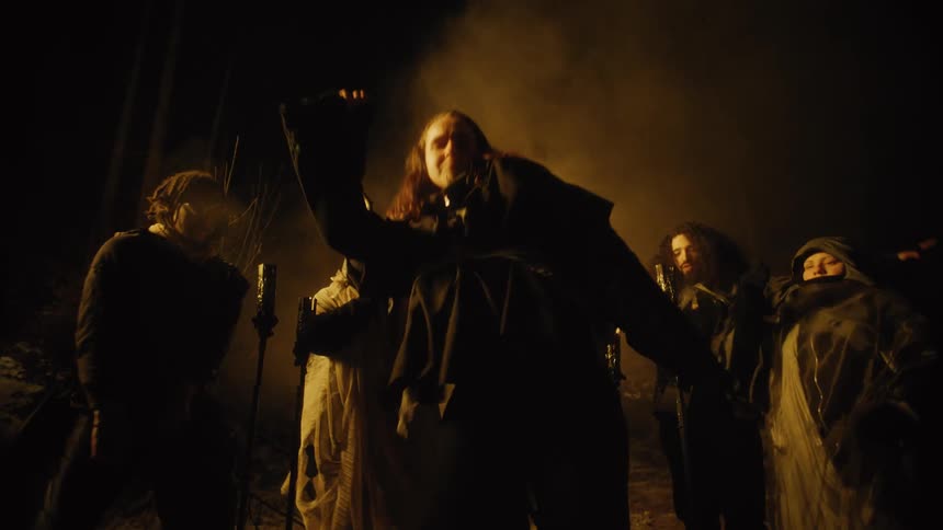 People dressed in historical clothing dance outside at night in front of tiki torches