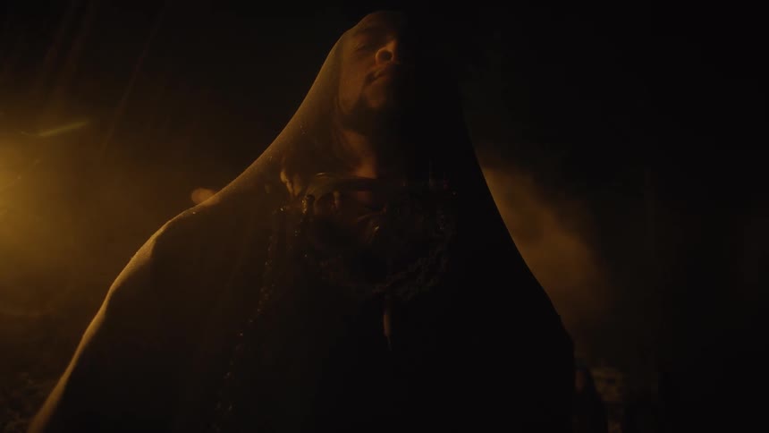 Man stands in shadowy foggy chamber with eyes closed wearing a shroud