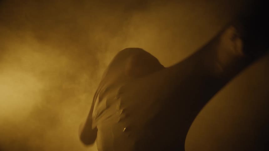 Person wrapped in thin fabric stretches and moves in yellow and brown smoke