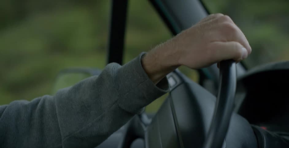 A white male has hand on the steering wheel of a car