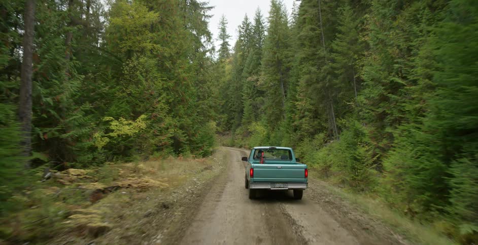 A truck drives down a gravel road through a wooded area