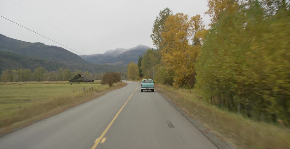 Older model pickup truck drives down rural highway through farmland in valley